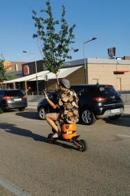 Sieht lustig aus, ist aber gegen die geltenden Vorschriften: E-Scooter-Fahrer sitzend auf einer Gasflasche mit gezücktem Handy.