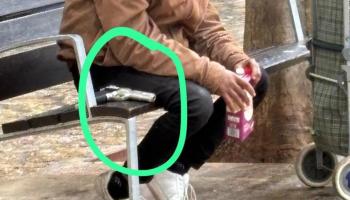 Ein Mann sitzt auf einer Bank auf der Plaça Nova de la Ferreria. Neben ihm liegt eine Waffe.