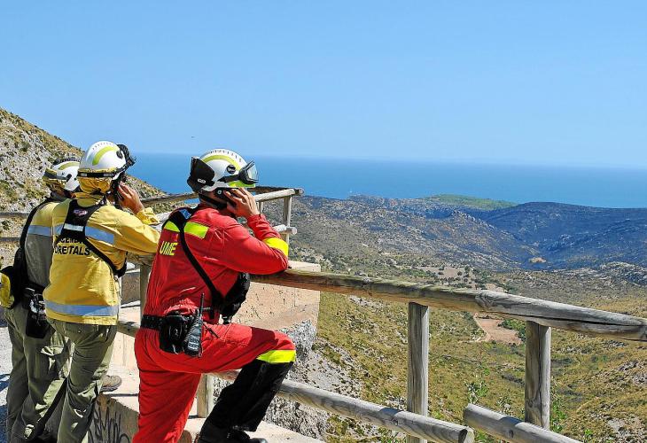 (Wieder) entspannte Feuerwehrleute blicken auf die verbrannte Hügelkette.